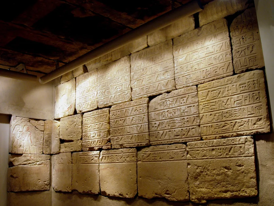 Sandstone Egyptian burial chamber walls with painted funerary scenes and hieroglyphic texts.