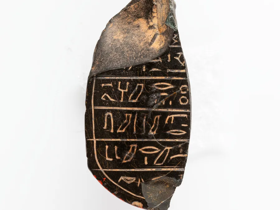 Stone fragment of an Egyptian human-headed heart scarab with inscribed underside.